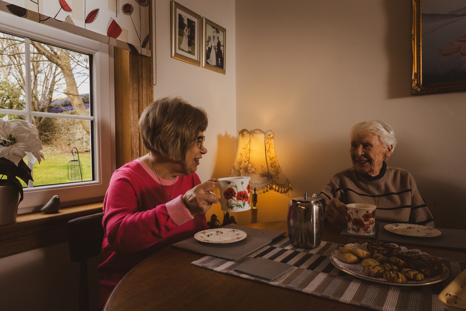 Two women chat over biscuits and tea.