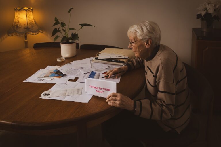 An older lady looks over various documents at a large wooden table